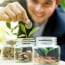 Businessman putting coin into the glass jar with young plant