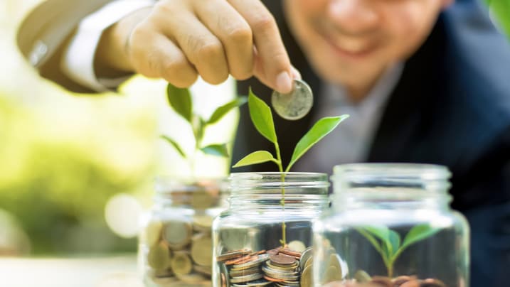 Businessman putting coin into the glass jar with young plant