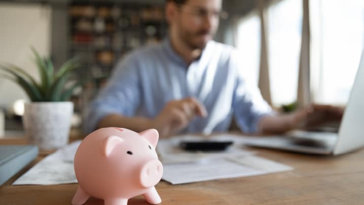 man working on his laptop with piggybank on desk