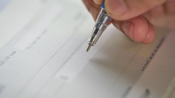 a person's hand writing a cheque